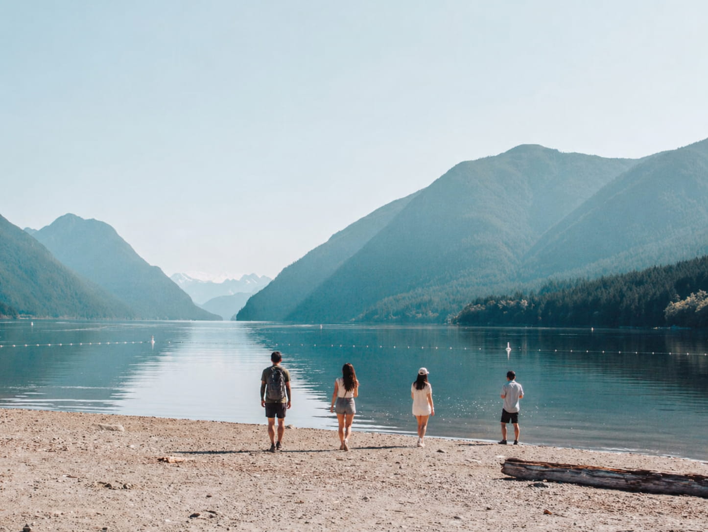 Group of friends standing on a rocky lakeshore with snow-capped mountains behind them